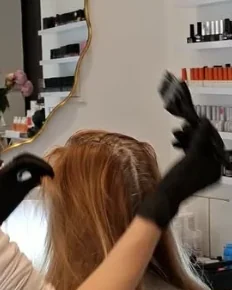 Haare werden im Salon gefärbt, im Hintergrund Regale mit Nagellack